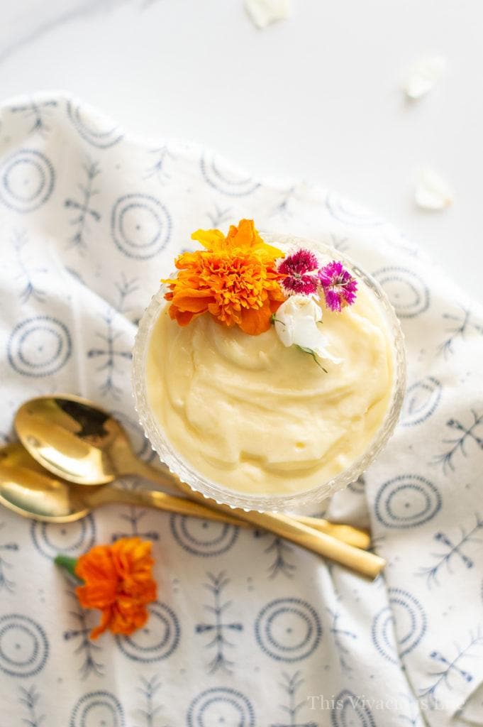 Overhead shot of vanilla pudding with edible flowers and gold spoons