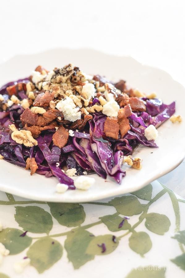 White plate with red cabbage salad topped with bacon and nuts