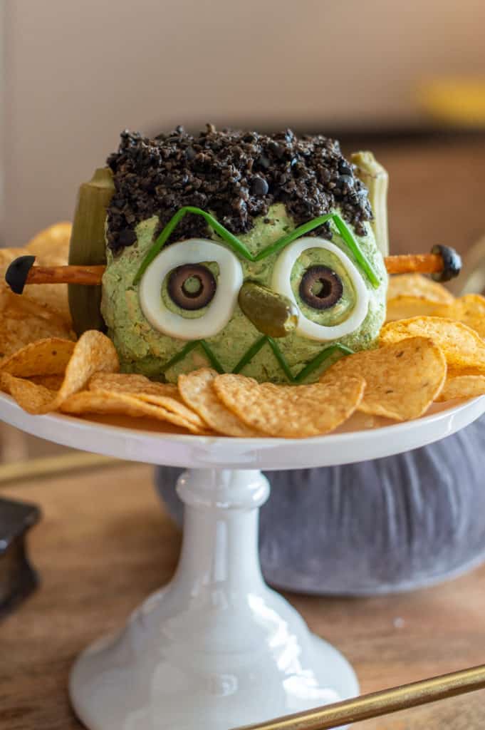 Frankenstein cheese ball with chips on a cake stand