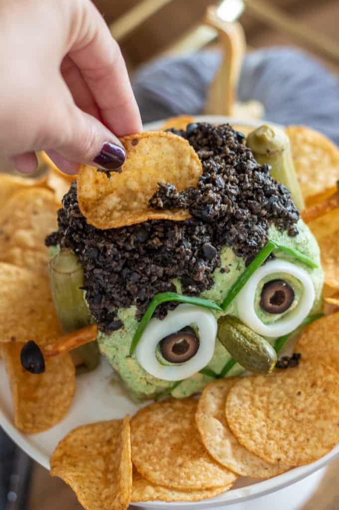 Chip being dipped into olive Frankenstein hair on Halloween cheese ball