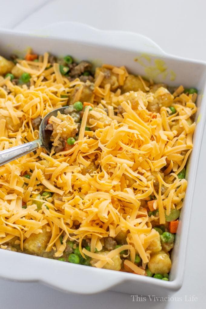 Tater tot caçarola ser mexido com uma colher e queijo por cima
