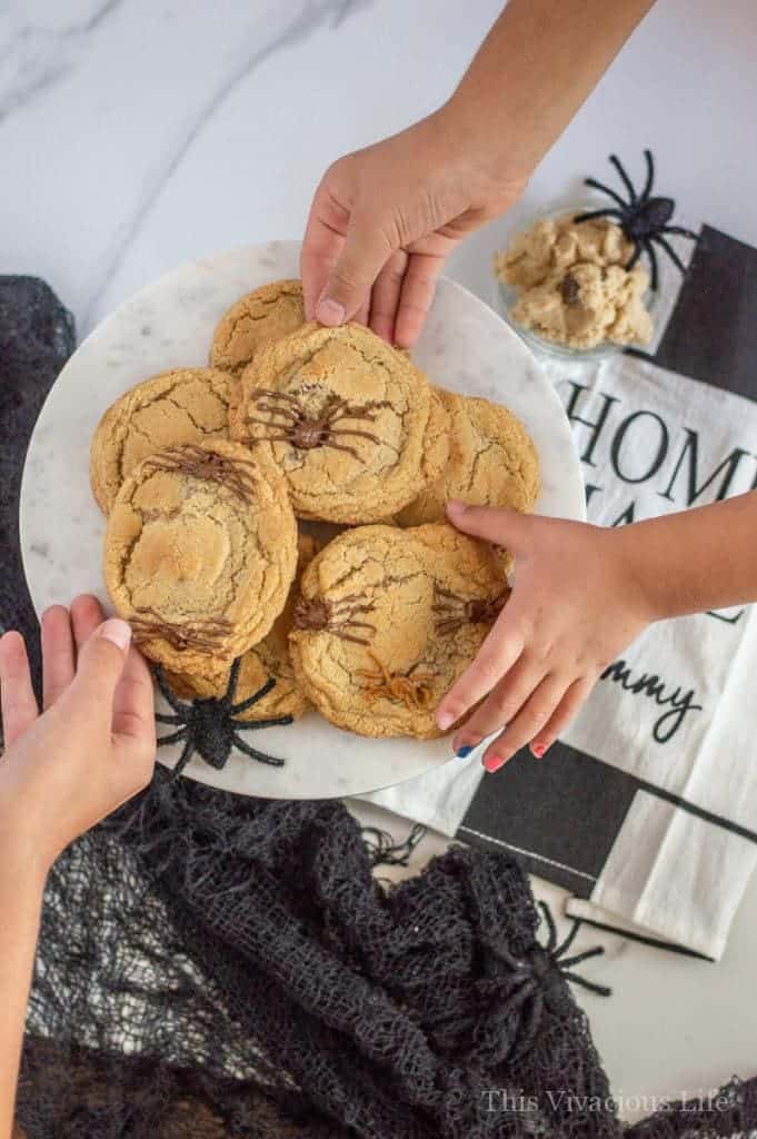 Three hands reaching for spider cookies on a platter