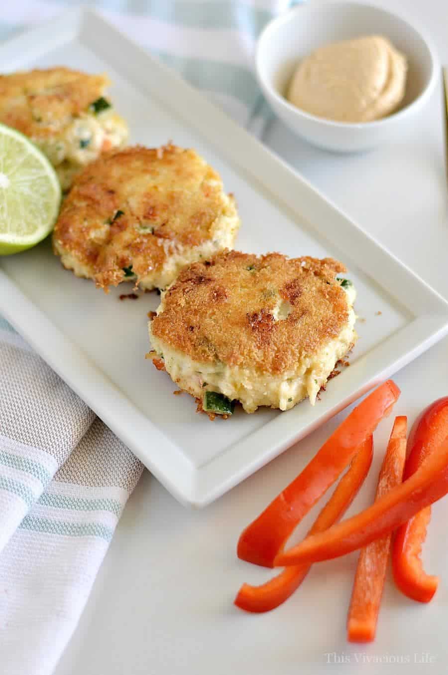 Three gluten-free crab cakes on a white plate with red peppers on the side
