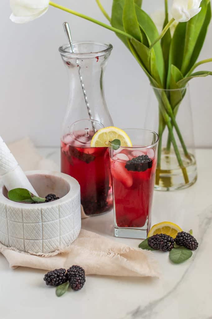 Glass and pitcher with blackberry lemonade near a tea towel