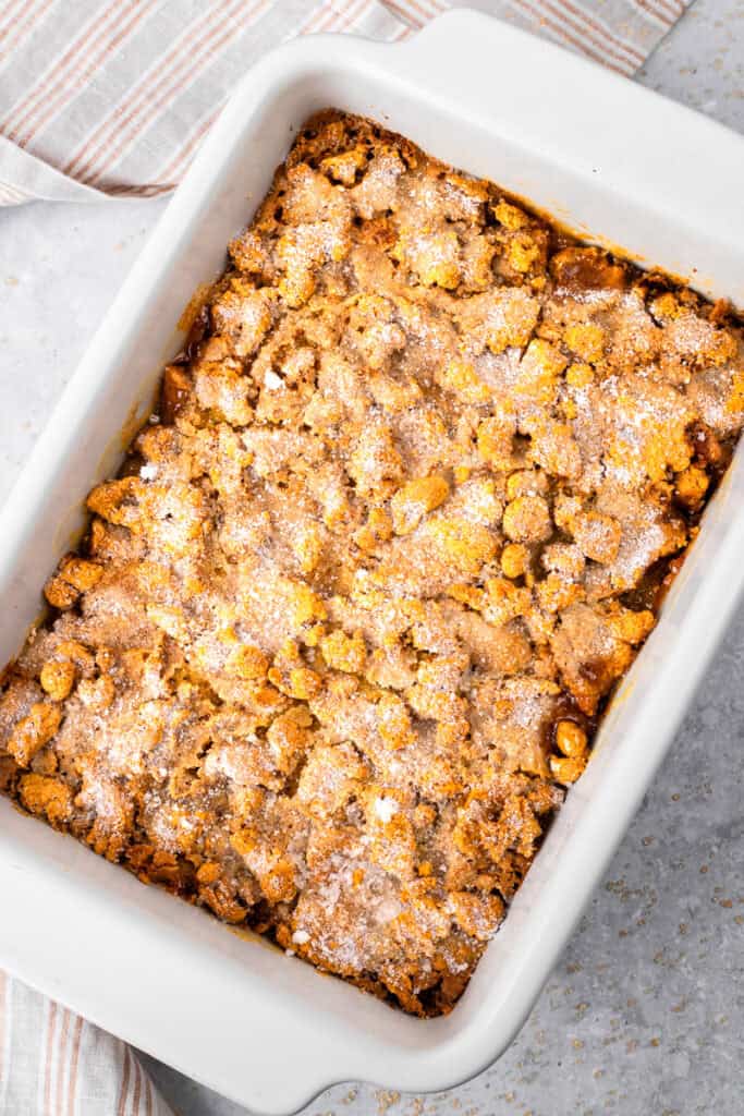 Top down image of peach cobbler in a casserole dish with gluten free topping, caramelized sugar on top, and golden peach filling