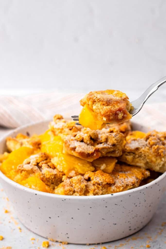 Side image of bowl of gluten free peach cobbler being scooped out with a metal spoon