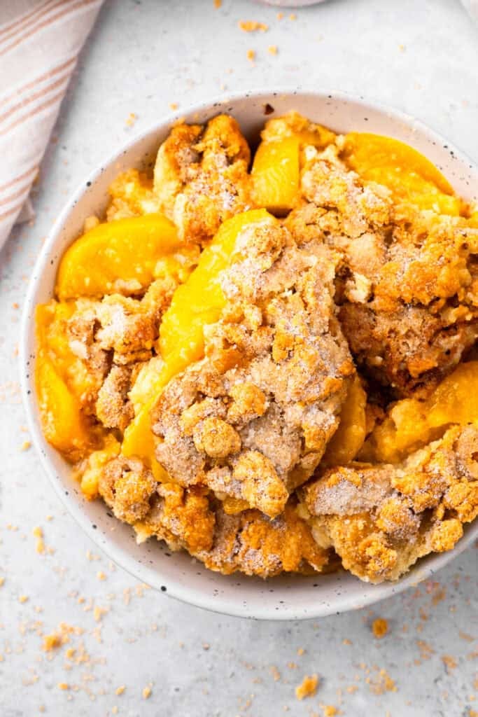 Top down image of a bowl of gluten free peach cobbler with fresh peach filling and golden brown crumbly top