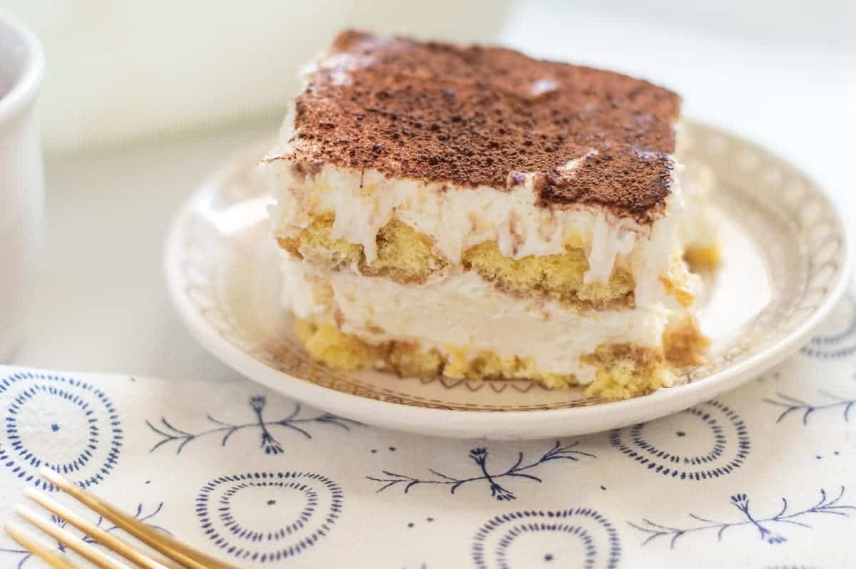 Gluten-free tiramisu on a small white plate, showing the layers of the tiramisu. There are two cream layers and two ladyfingers layeres.