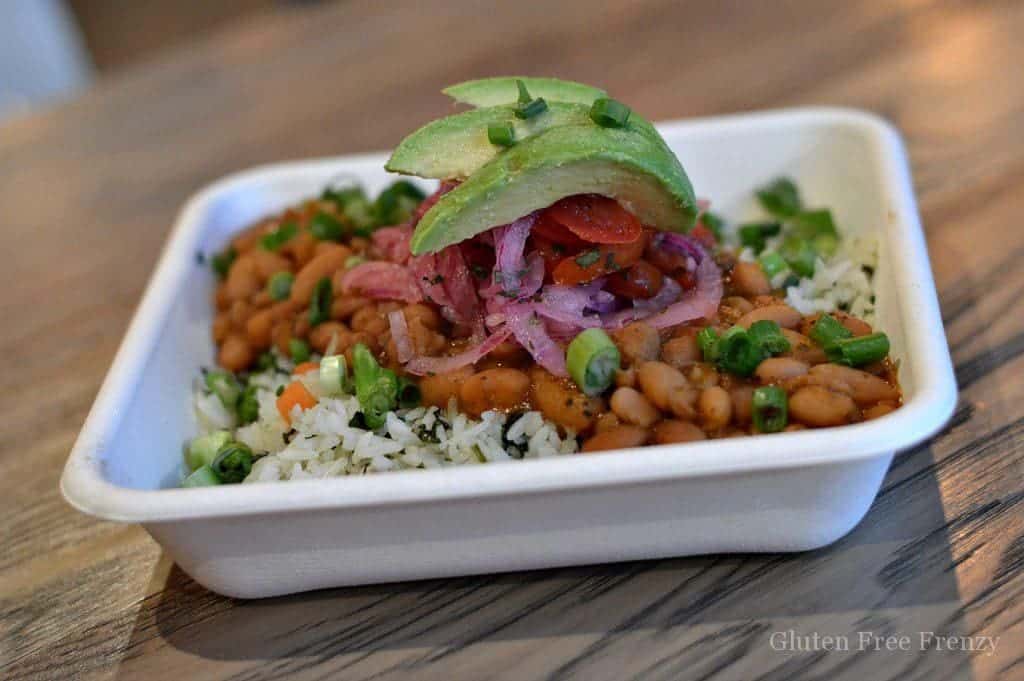 Rice, beans with avocado on top in a paper square dish