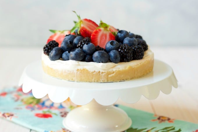 A cheesecake with berries on a white cake stand