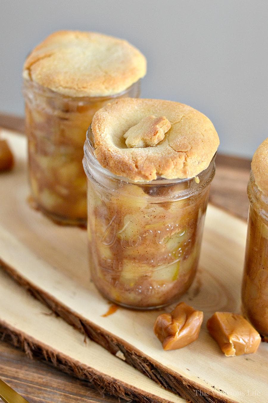 Two apple pies in glass mason jars. The crust is golden and there is a flower made of the crust on top of one of the pies.