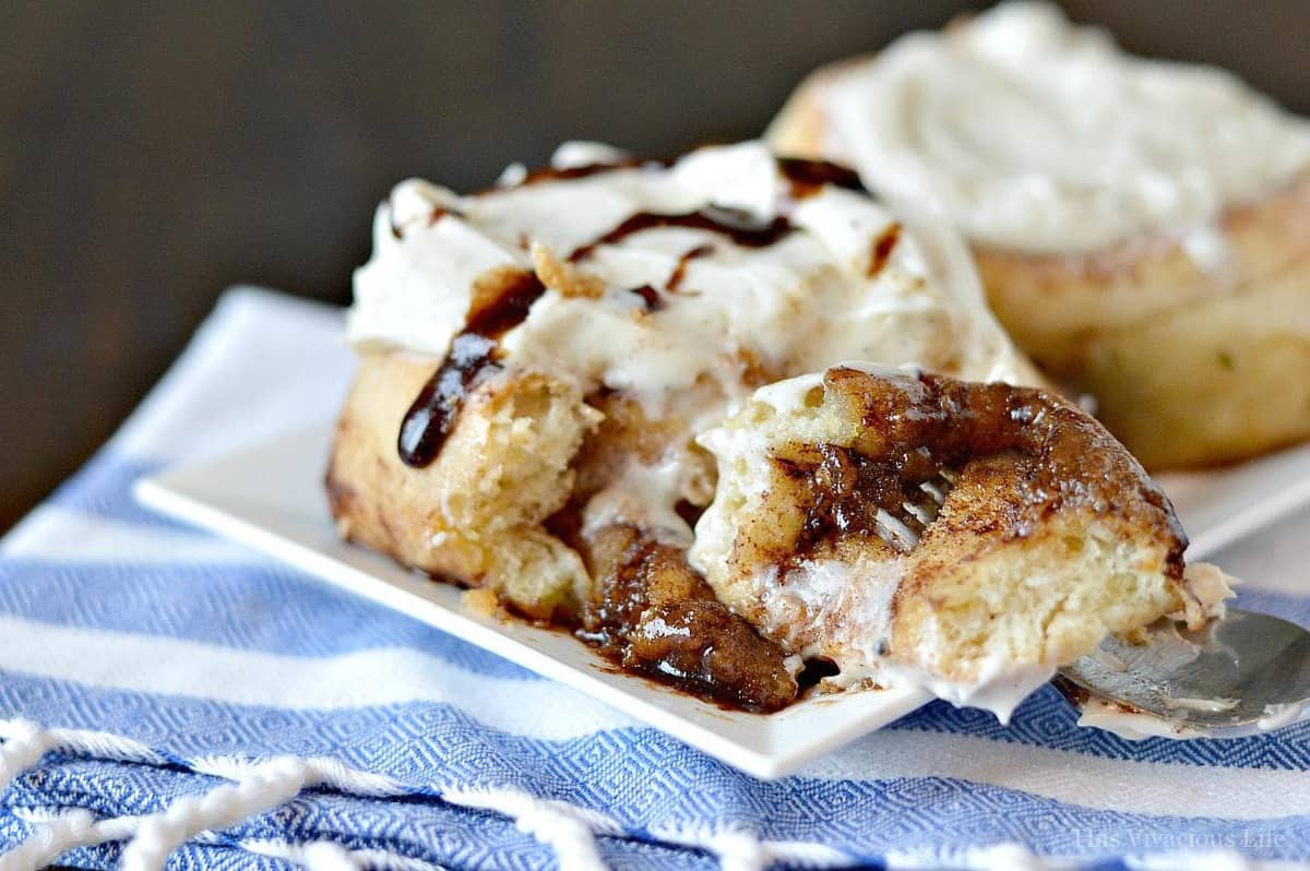 Gooey gluten-free cinnamon rolls topped with cream cheese frosting and brown sugar drizzle with a piece on a fork. 