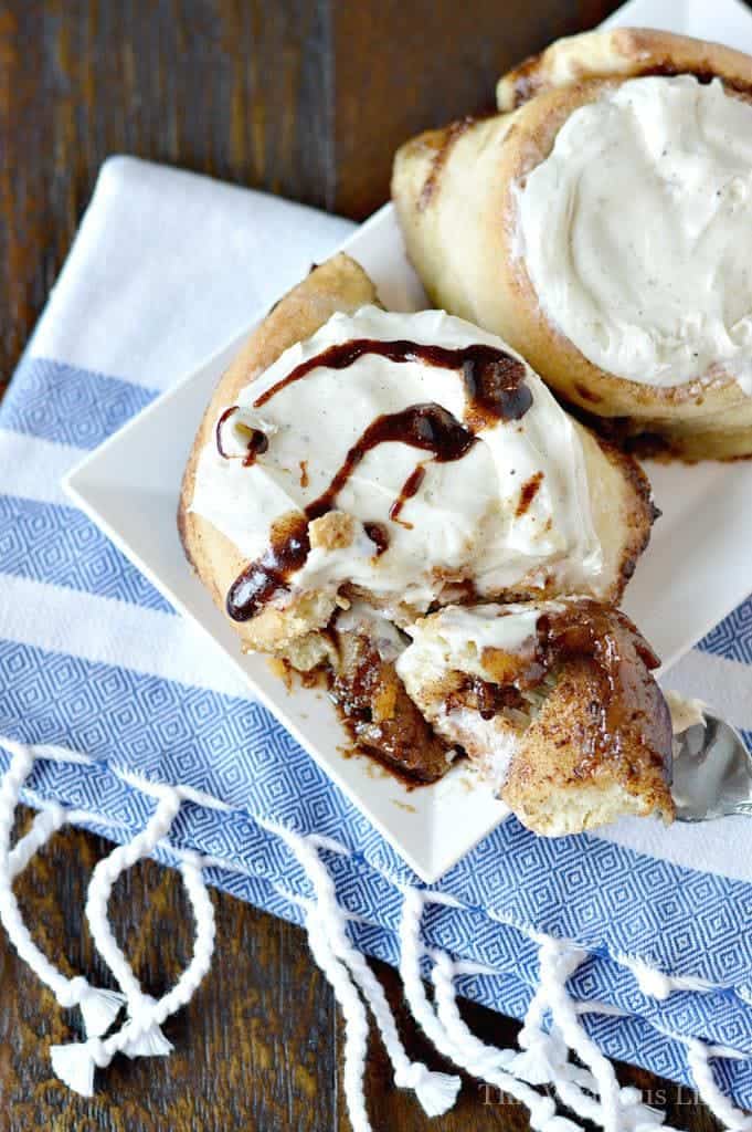 Overhead photo of gluten-free cinnamon rolls on a white plate, on top of a blue and white towel, being cut into with a fork