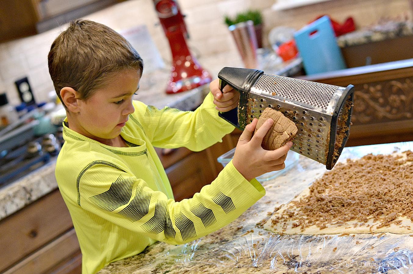 Frozen brown sugar butter cinnamon roll filling being grated by a little boy onto the dough. 
