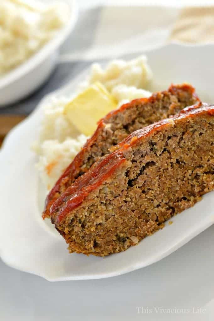 Two slices of meatloaf on a white plate with mashed potatoes