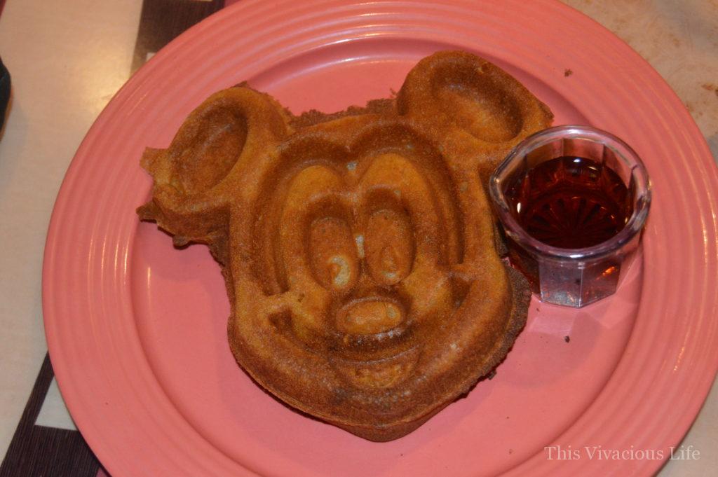 Gluten-free Mickey Mouse waffle and syrup on a coral plate