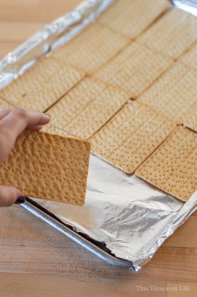 christmas crack step by step instructions with hand putting crackers on tinfoil lined baking sheet