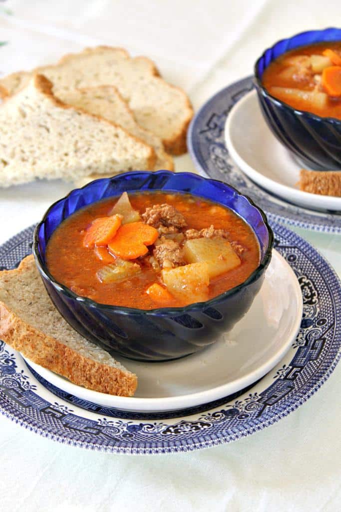 Instant Pot hamburger soup in a white bowl with bread next to it