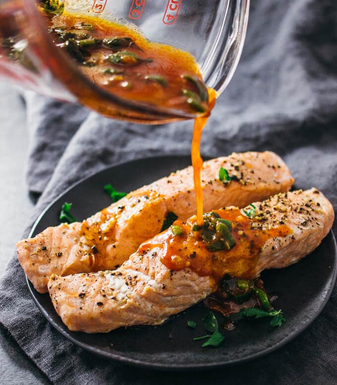 Two salmon filets with sauce being poured on