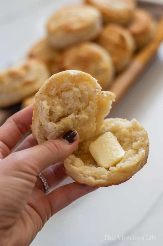 One biscuit split with butter in a hand