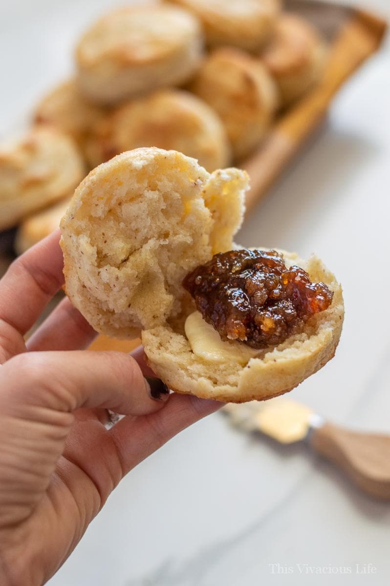 A split biscuit with butter and fig jam being held