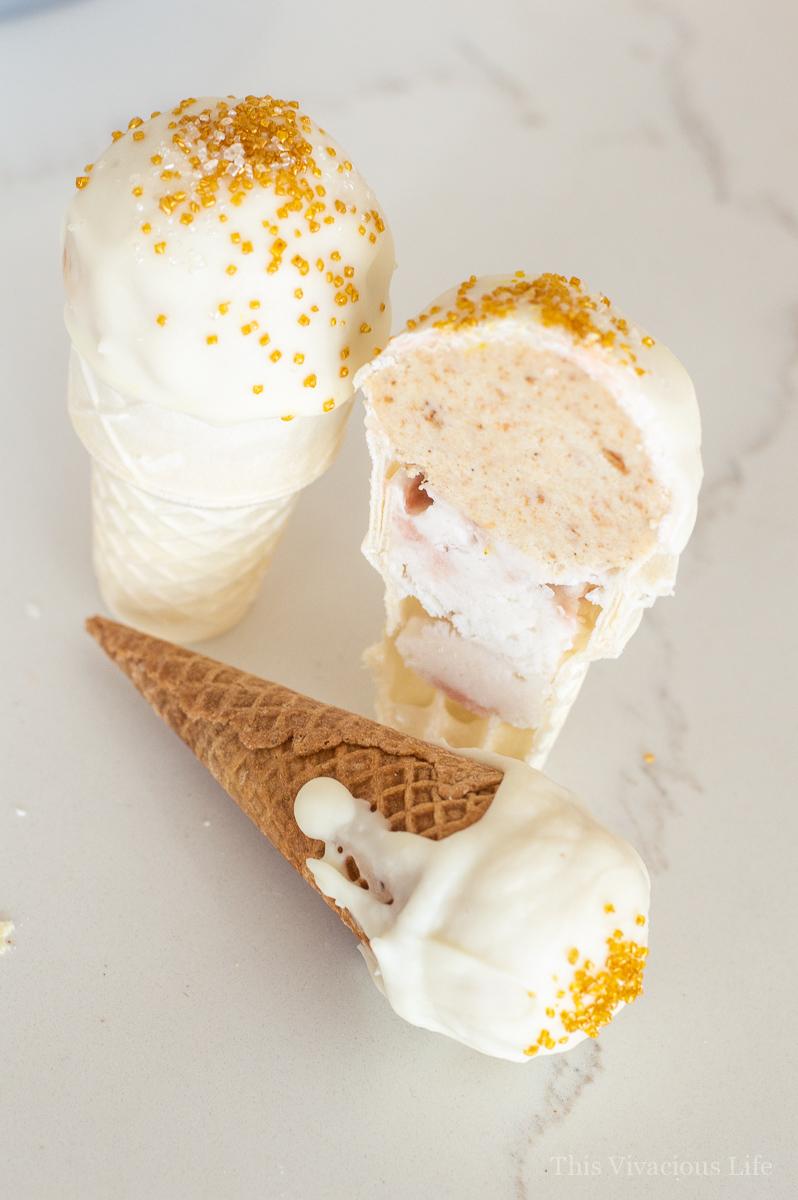 Gluten-Free Ice Cream Cake Pops | These gluten-free ice cream cake pops are so great for summer. They take a fun spin on a classic ice cream cone. || This Vivacious Life #glutenfree #cakepops #dessert #summerdessert #glutenfreedessert Three ice cream cake pops, one cut in half to see in the middle, and one laying on the ground with a waffle cone.