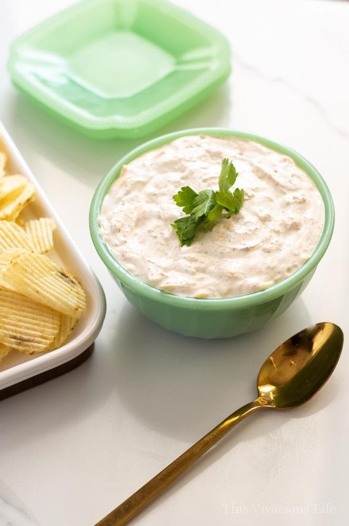 A bowl of Sour Cream Dip with Chives on Top next to Potato Chips and a Spoon
