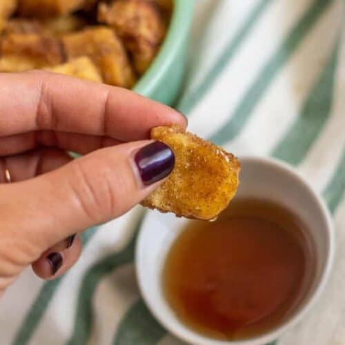 French toast bite in hands dipped in syrup