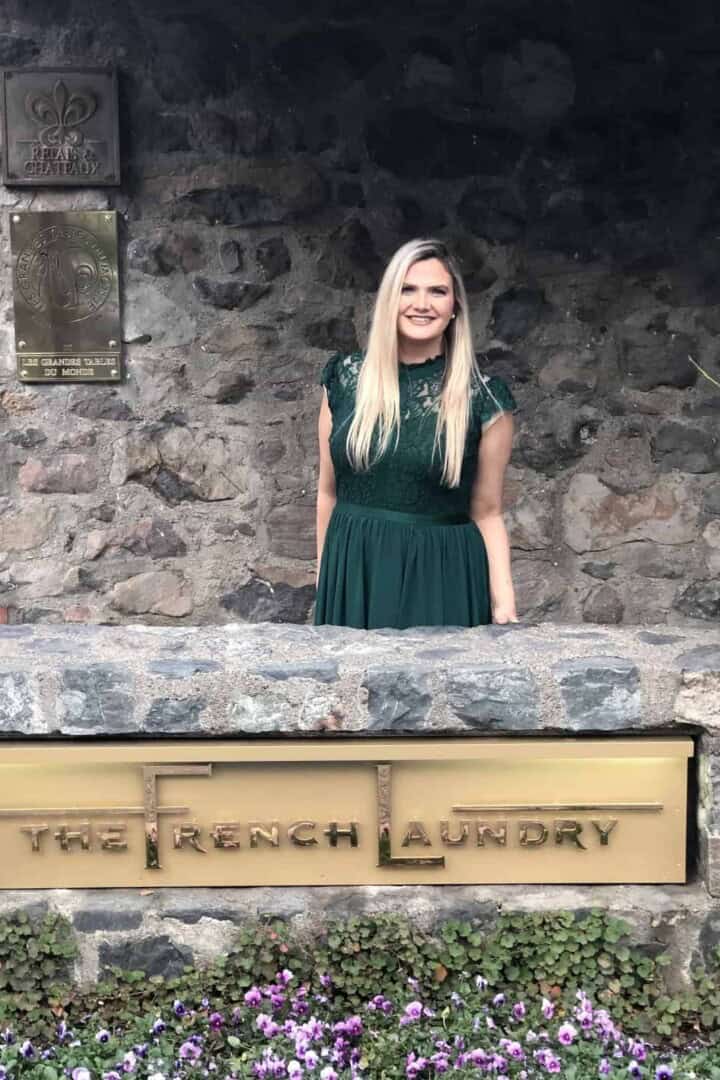 Chandice Probst standing by the rock wall and The French Laundry sign in a green dress.