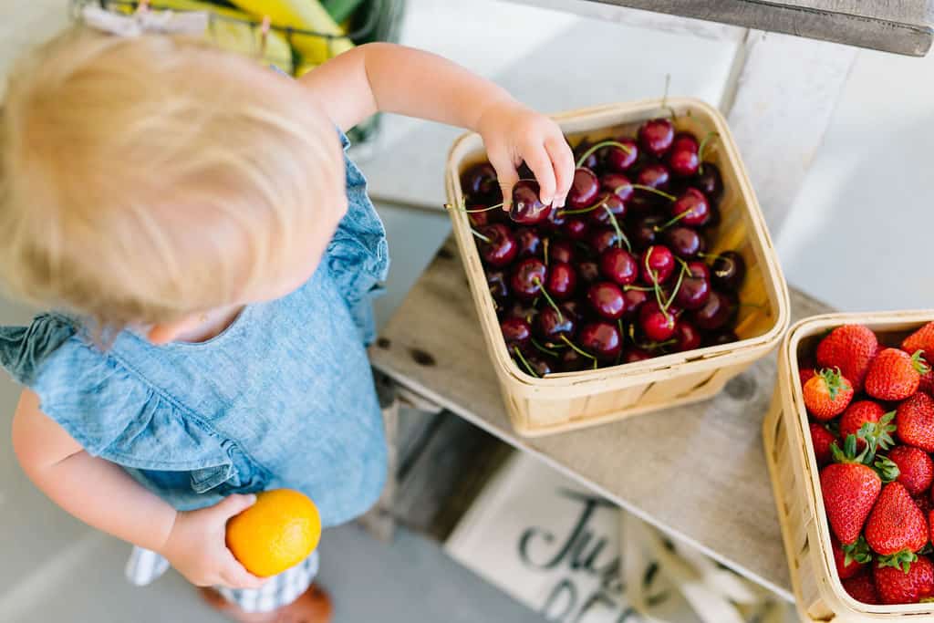 Little girl picking cherries out of a basket