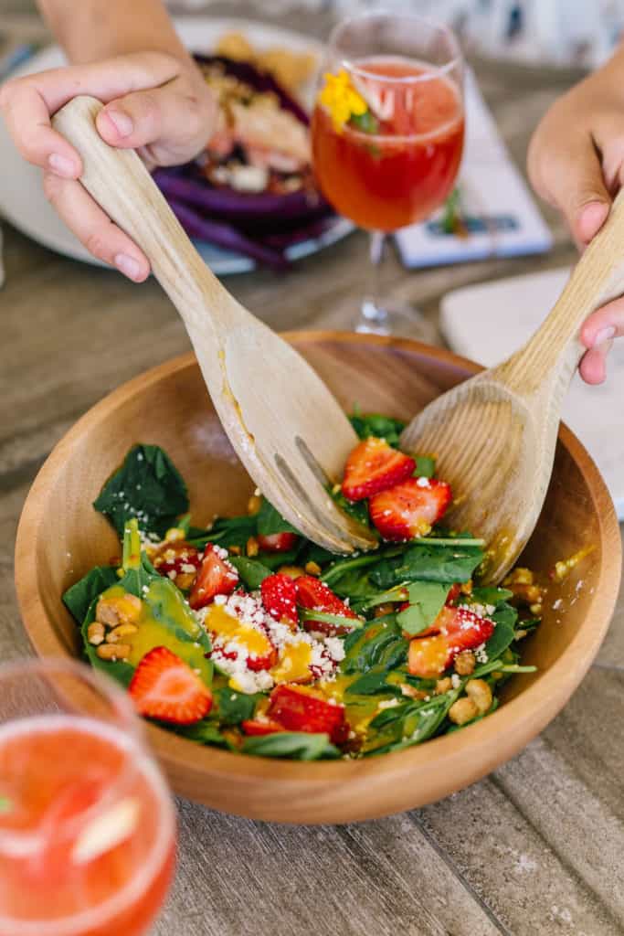 Salad being tossed with wood utensils