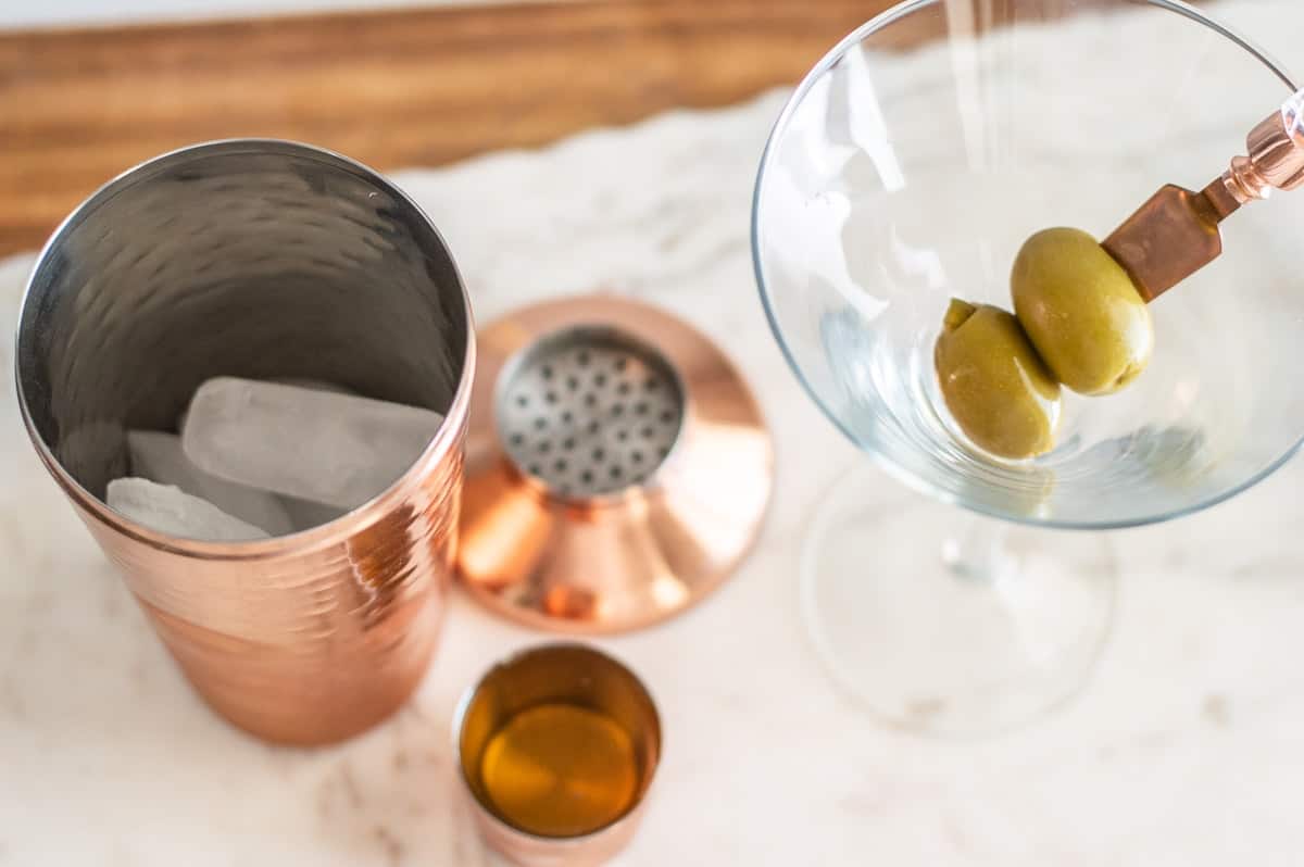 Tumbler with ice and martini glass with green olives