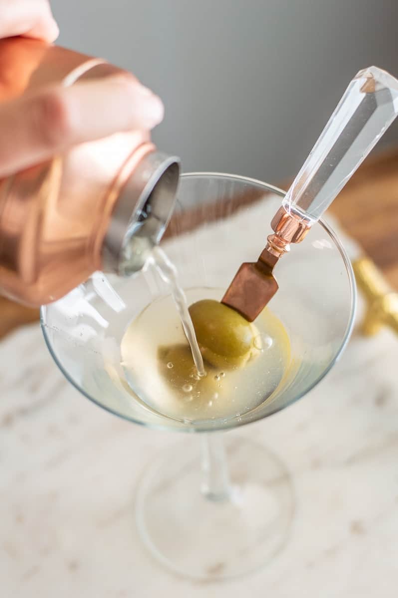Non-alcoholic vodka being poured into a martini glass with olives