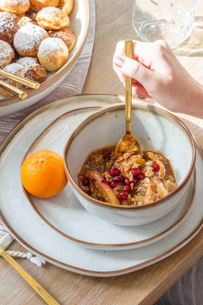 Bowl filled with instant pot apple crisp and pomegranates with an orange on the side