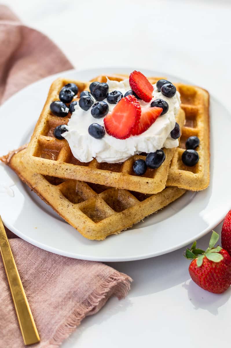 Three square waffles on a white plate with berries