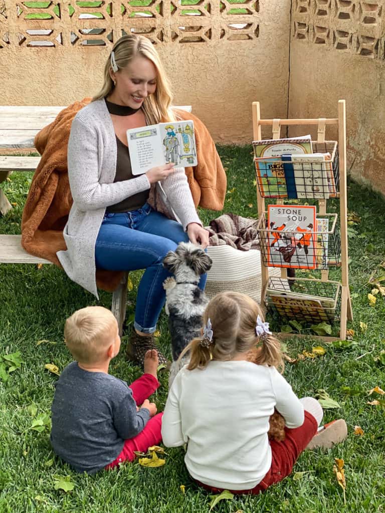 Lady reading books outside to two kids