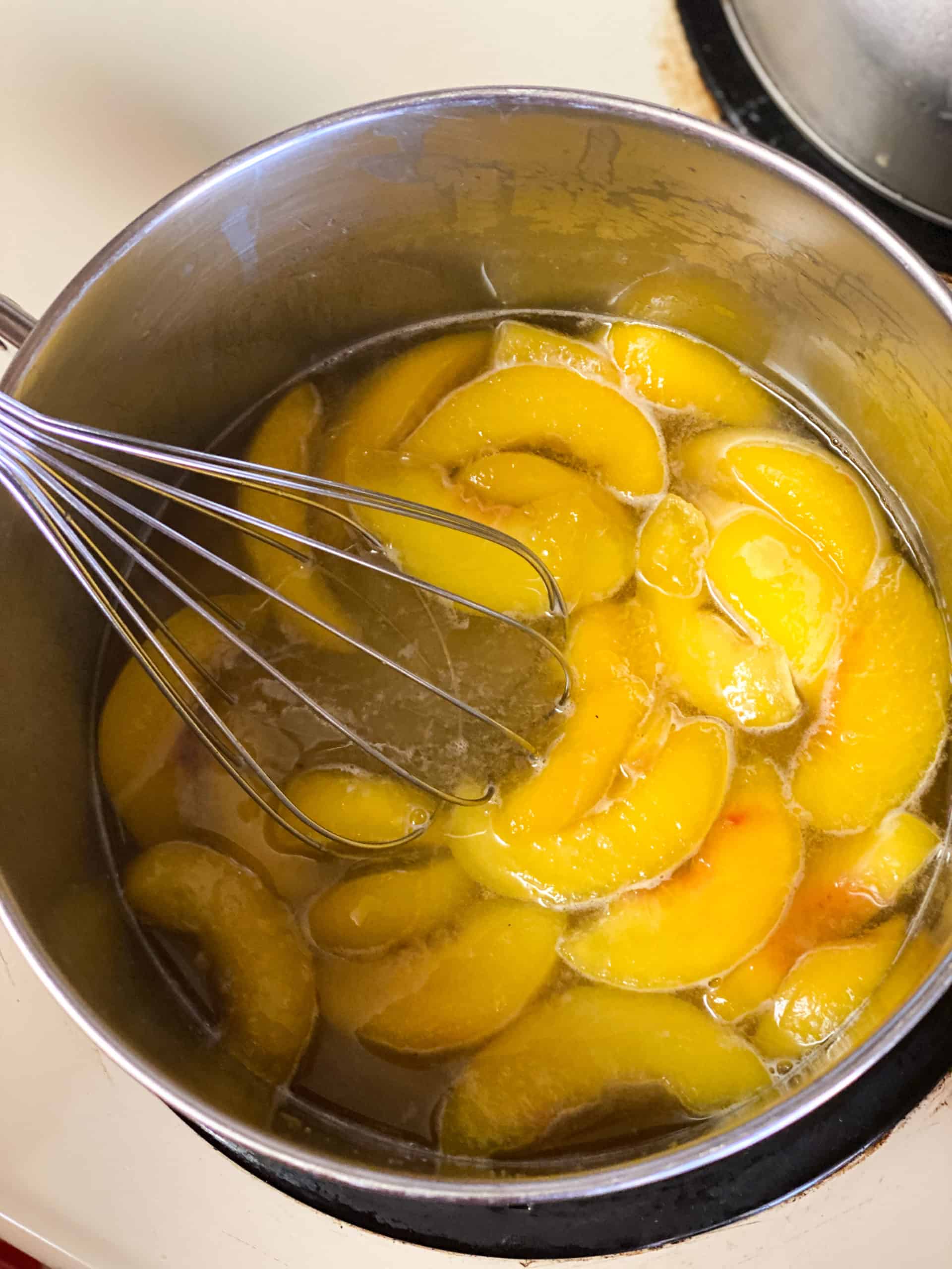 Peaches in sugar water being stirred with a whisk
