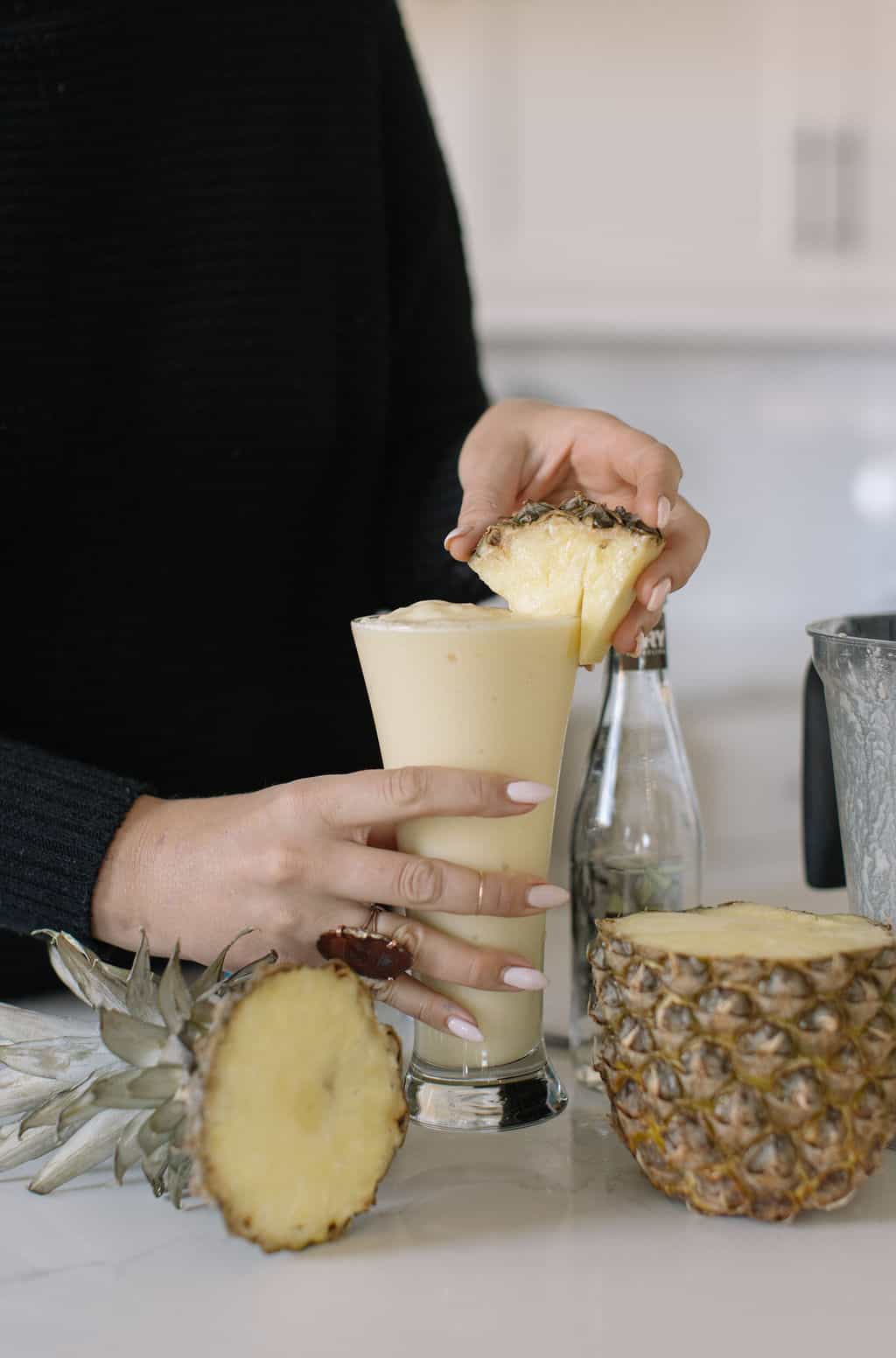 hands holding glass of pina colada mocktail in a glass with pineapple wedge