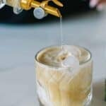 This white Russian mocktail is in a glass with simple syrup being poured into it
