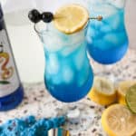 Blue lagoon mocktail in a hurricane glass with lemon and cherries
