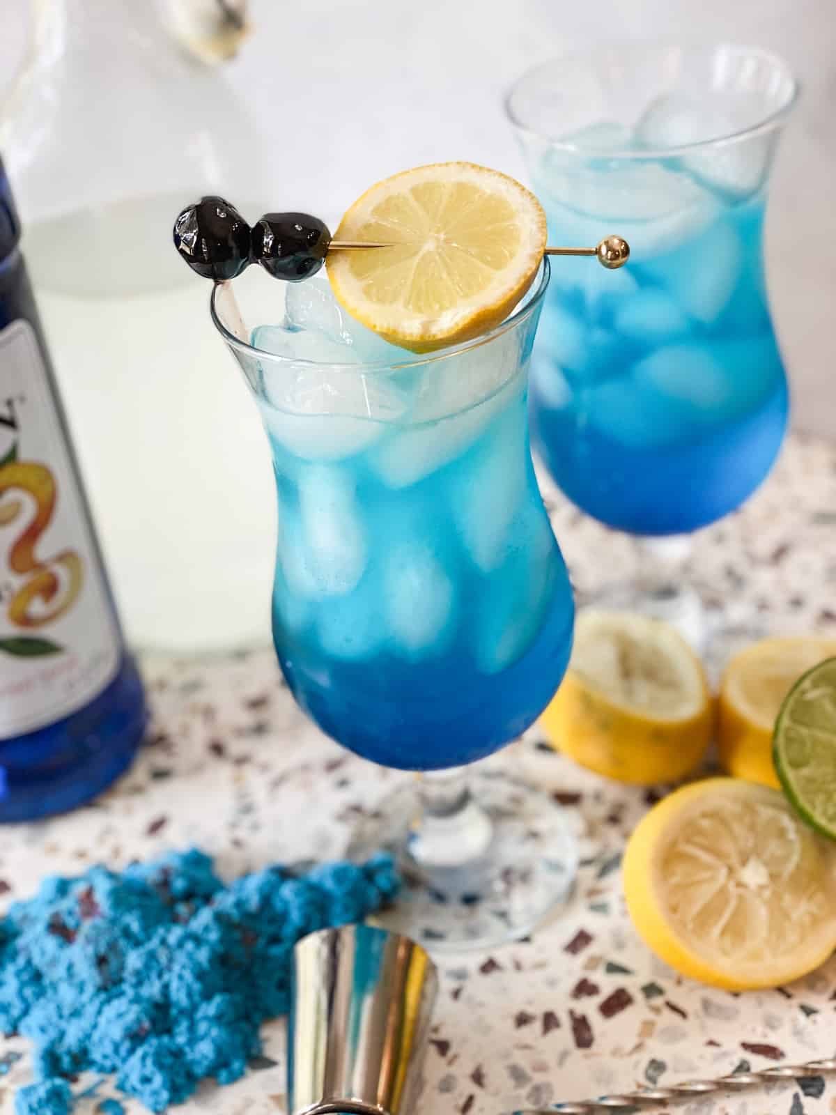 Blue lagoon mocktail in a hurricane glass with lemon and cherries