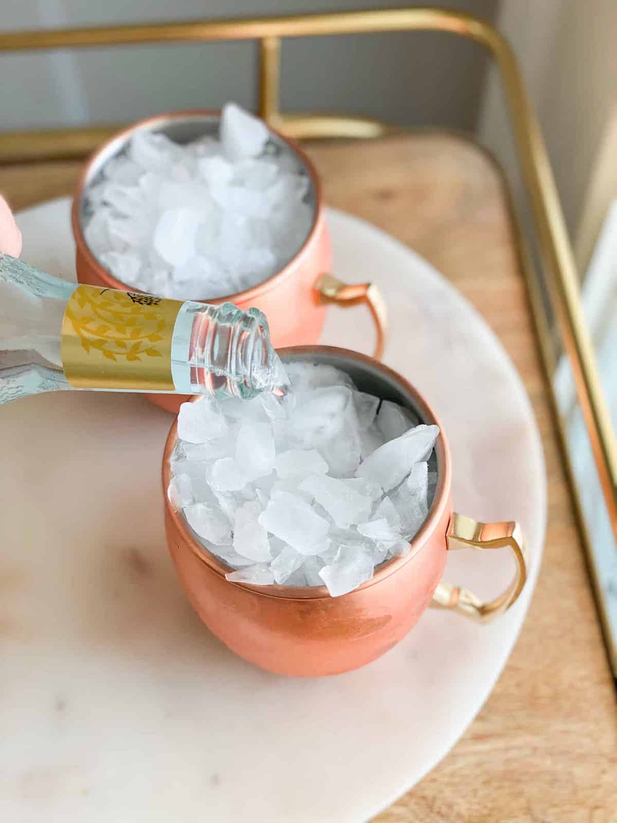 Ice in a copper cup with ginger beer being poured into a cup