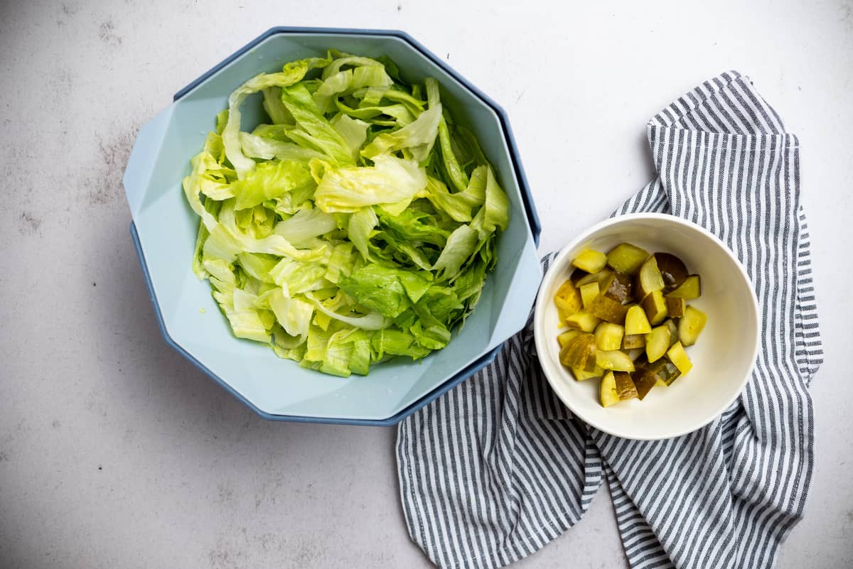 Lettuce in a blue bowl and chopped pickles in a little bowl