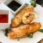 Frozen egg rolls in air fryer on a white plate with sauces