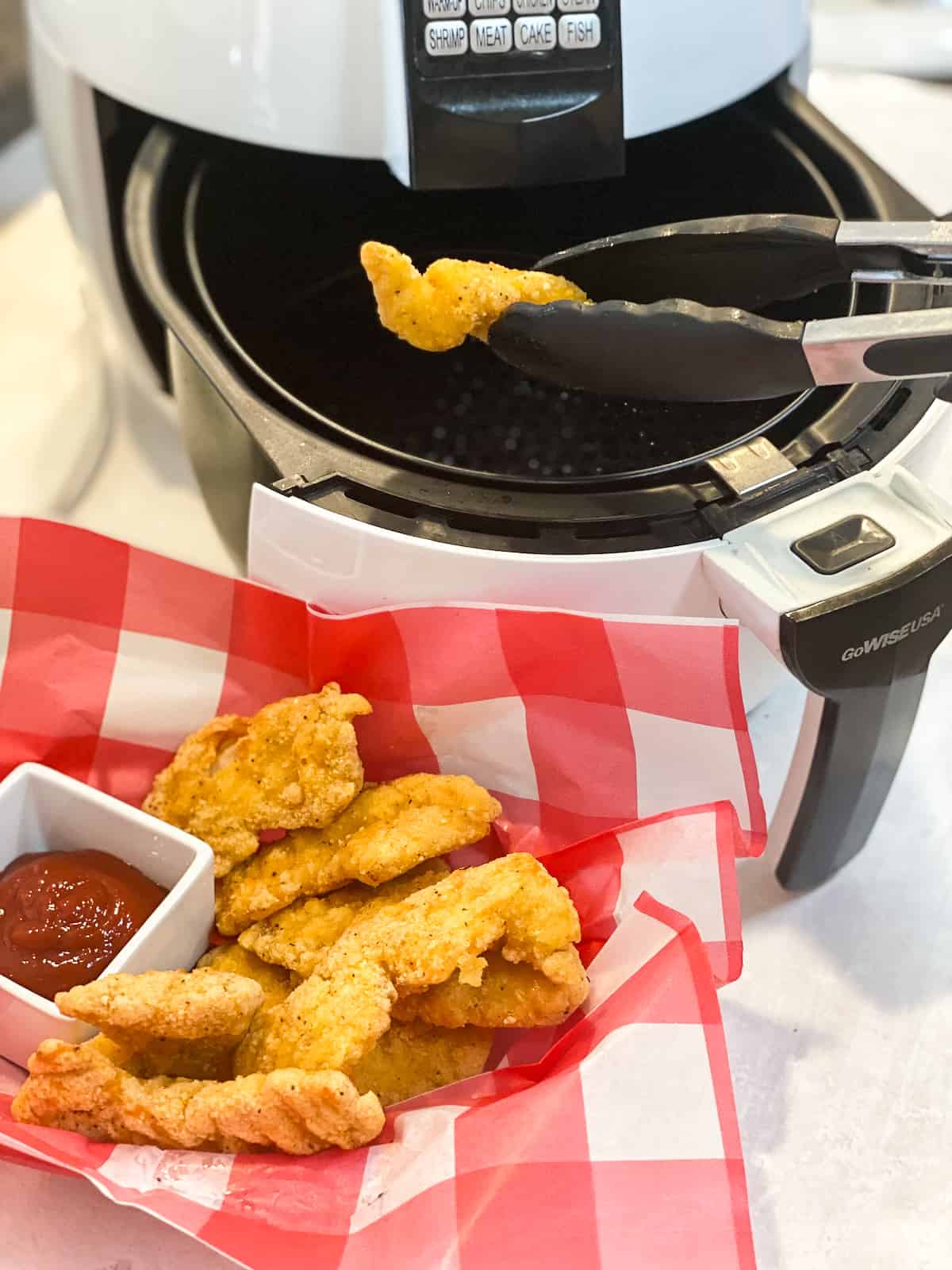 Frozen chicken tenders in air fryer coming out onto a checkered plate