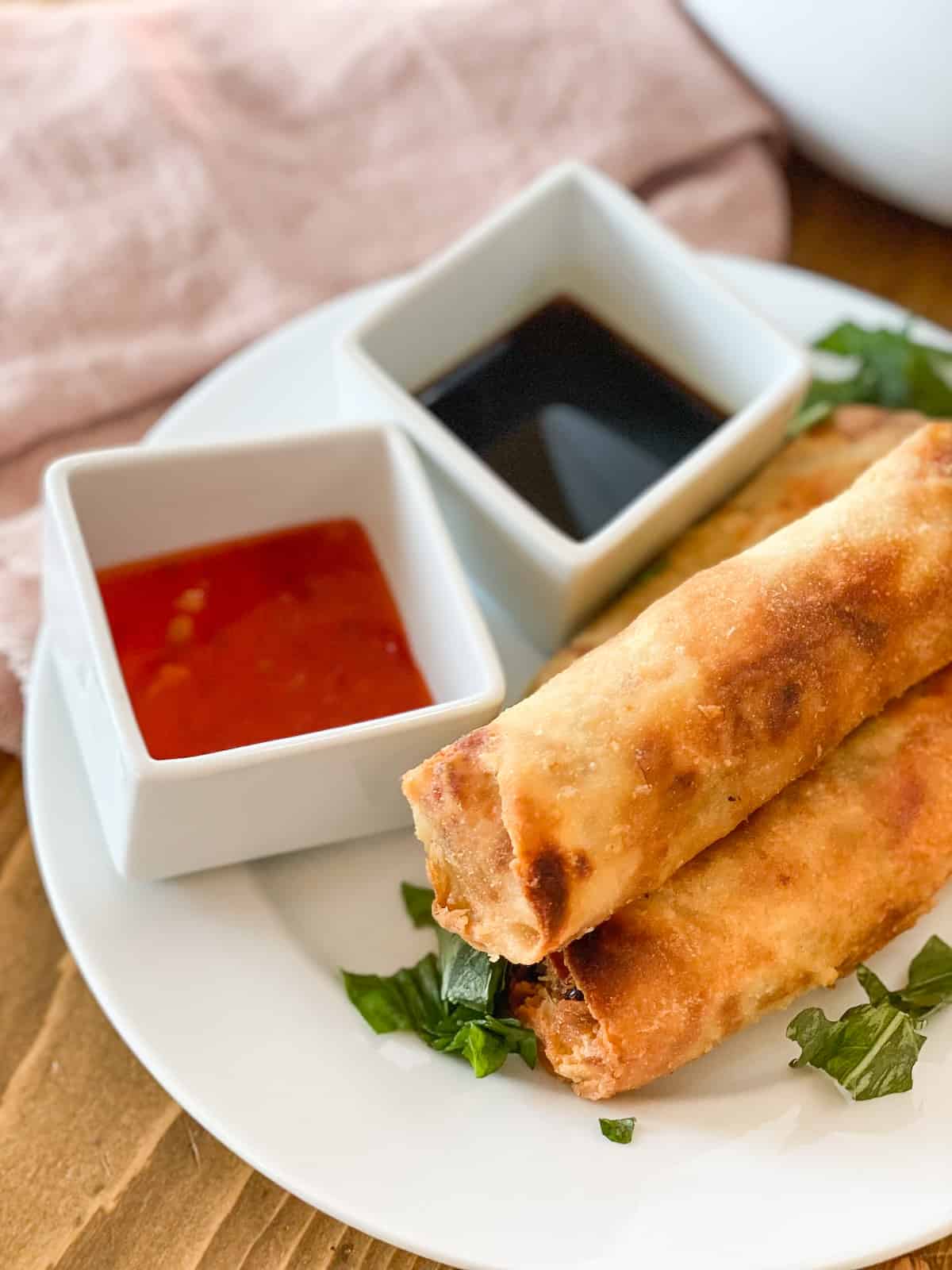 Frozen egg rolls in air fryer on a white plate with sauces