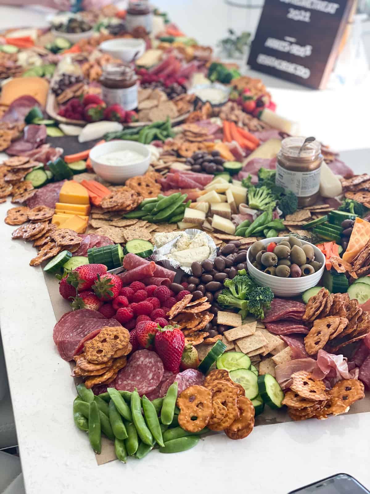 Large Grazing Table on butcher paper with pretzels, cheeses, vegetables, fruits, cheeses, meats, and more snacks in small bowls. 