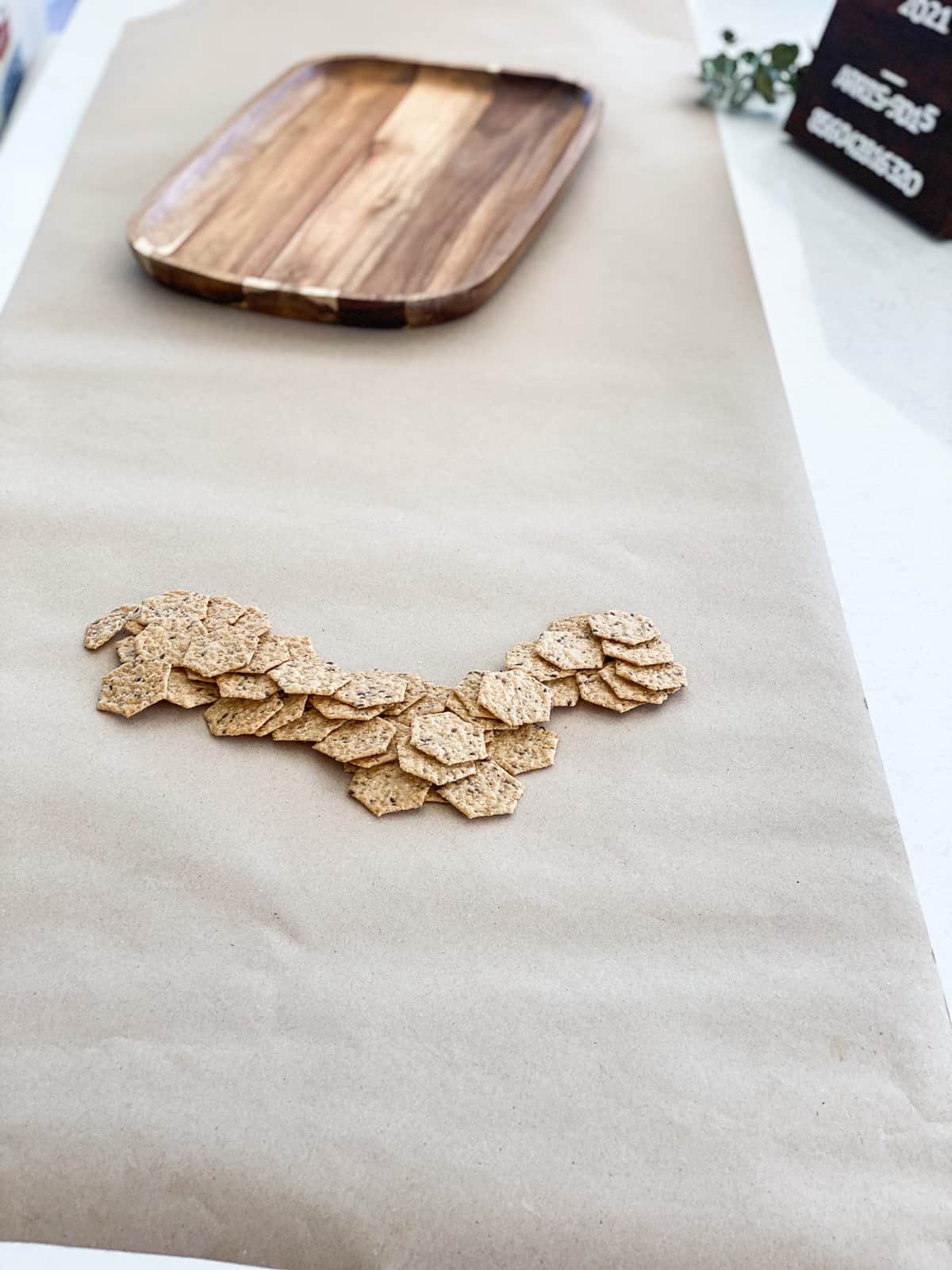 Butcher paper with a row of crackers and small charcuterie board in the middle. 