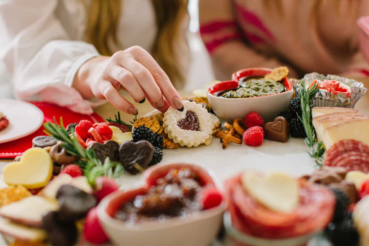 Hand picking up a heart cookie on a Valentines charcuterie board