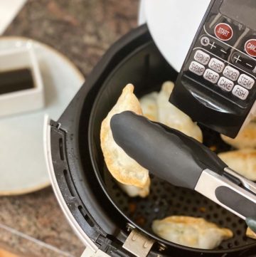 Frozen Pot Stickers in Air Fryer with tongs being pulled out